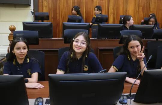 Alumnas sonriendo a la cámara sentadas en la sala de sesiones del senado